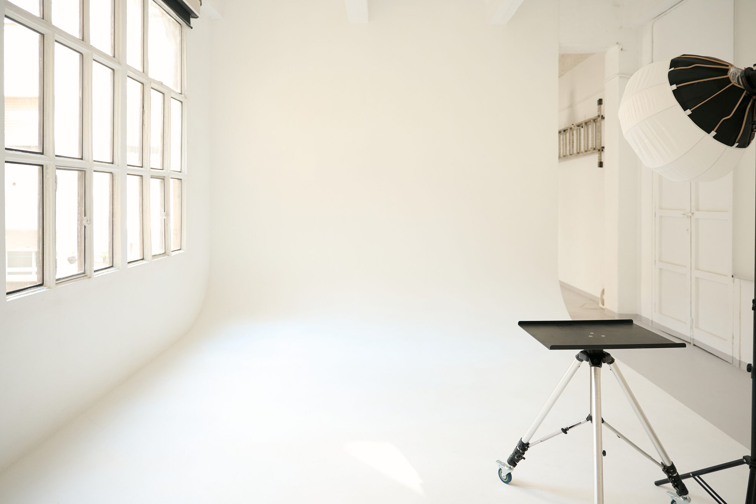 Bright, spacious photo studio with white cyclorama wall, professional lighting equipment, and a large window providing natural light